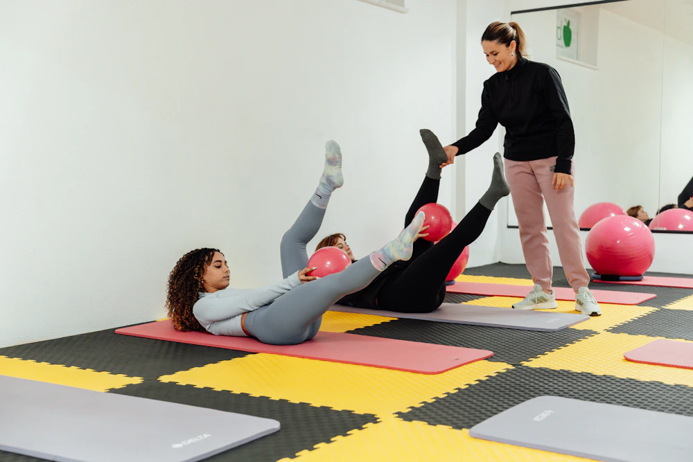 An instructor guiding a student through a mat exercise in a bright studio