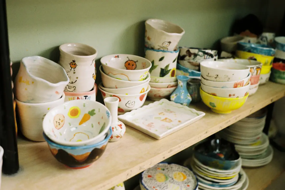 Shelves stacked with handmade bowls, cups and plates in a busy pottery studio