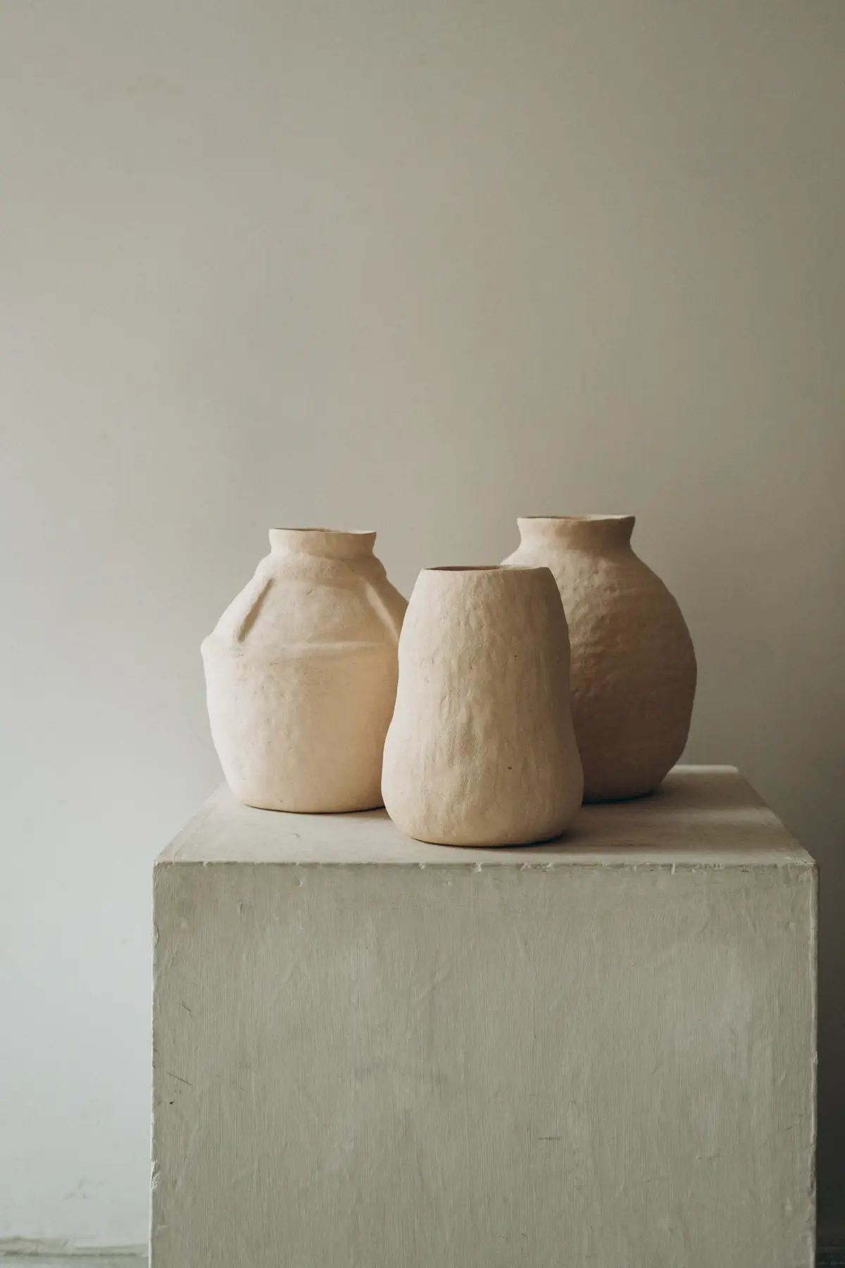 Three hand-pinched sand-coloured stoneware vases on a plinth