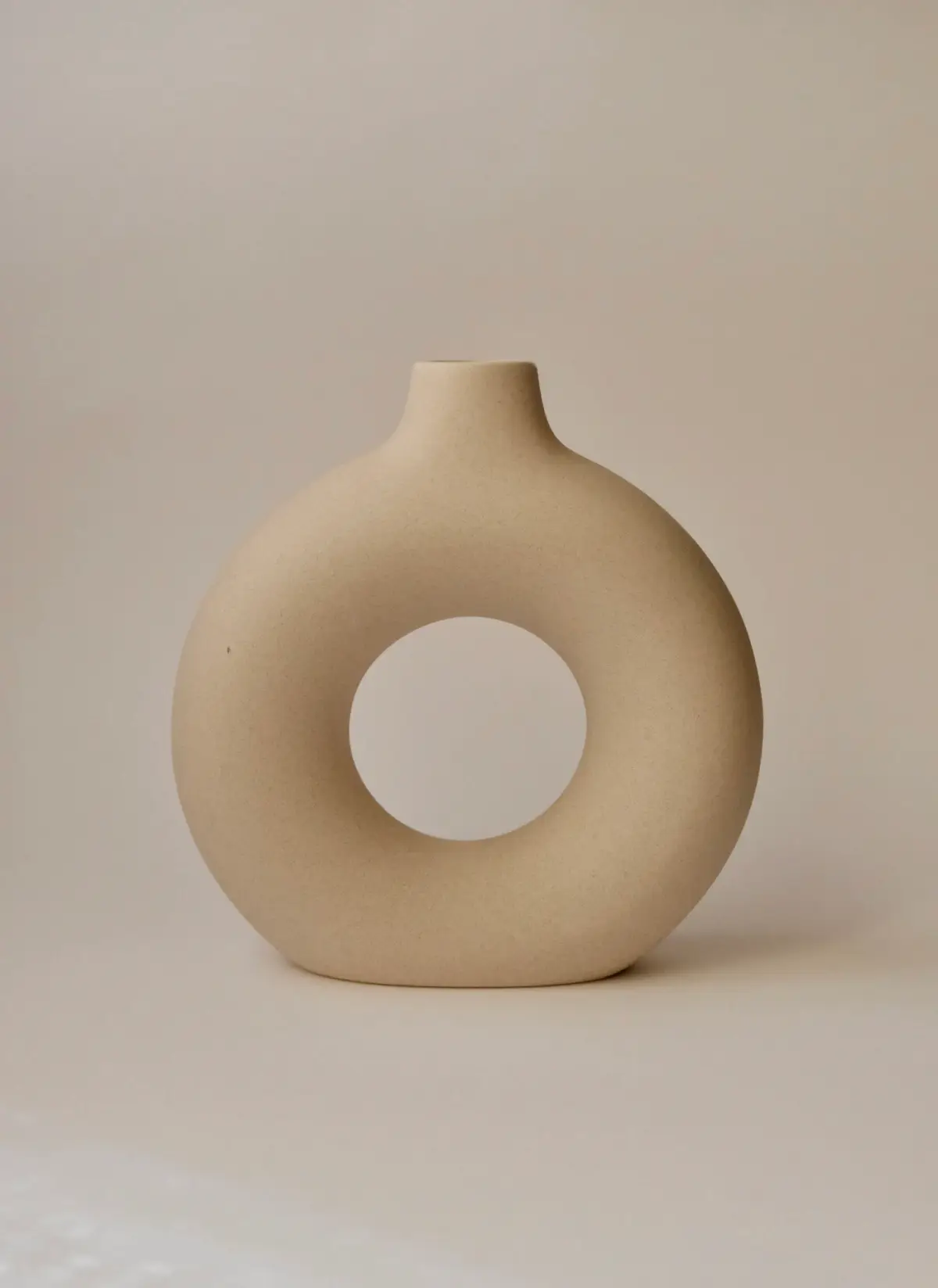 A ring-shaped matt oat stoneware vase on a cream background