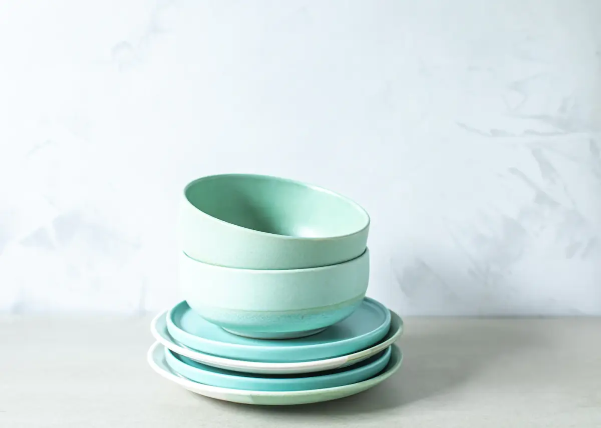 Stacked sea-glass glazed bowls and plates on a white table