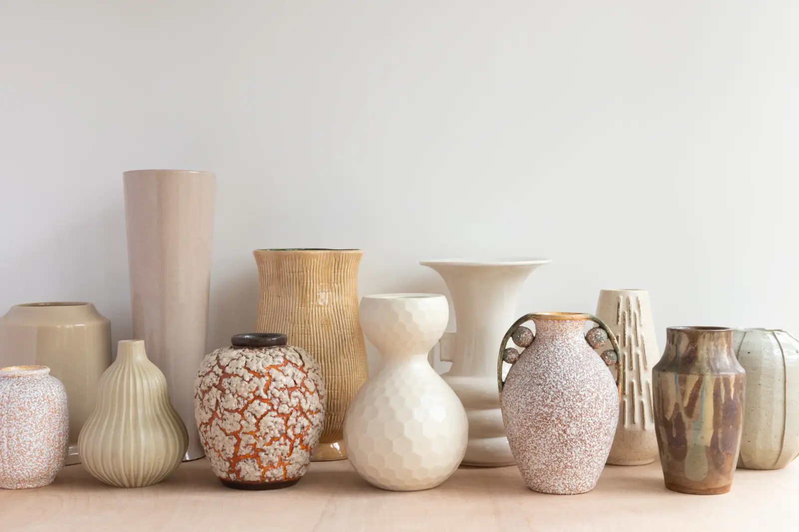 A row of handmade stoneware vases in cream, sand and terracotta glazes on a wooden shelf