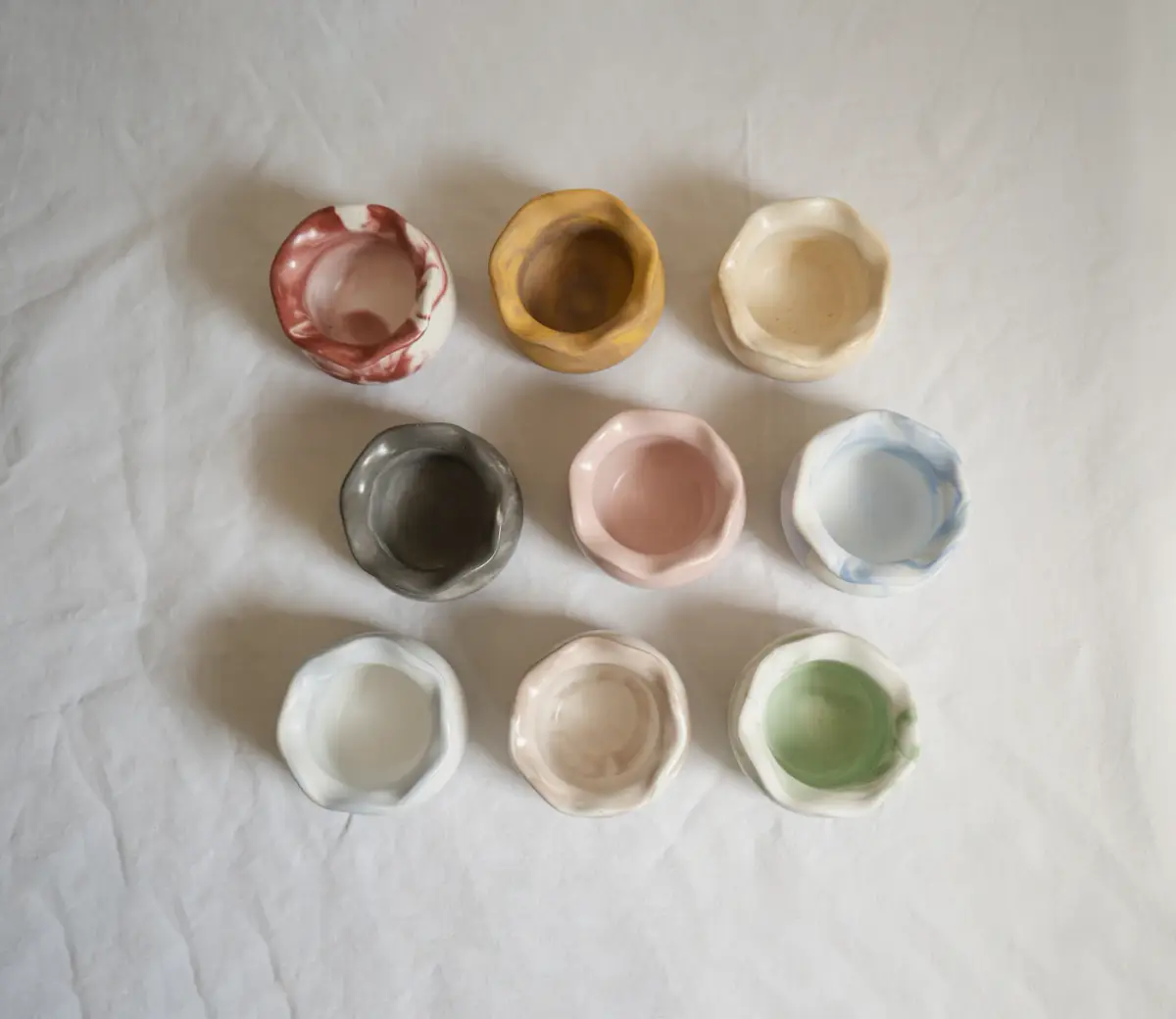Nine small hand-pinched dishes in pastel and earth glazes on white linen