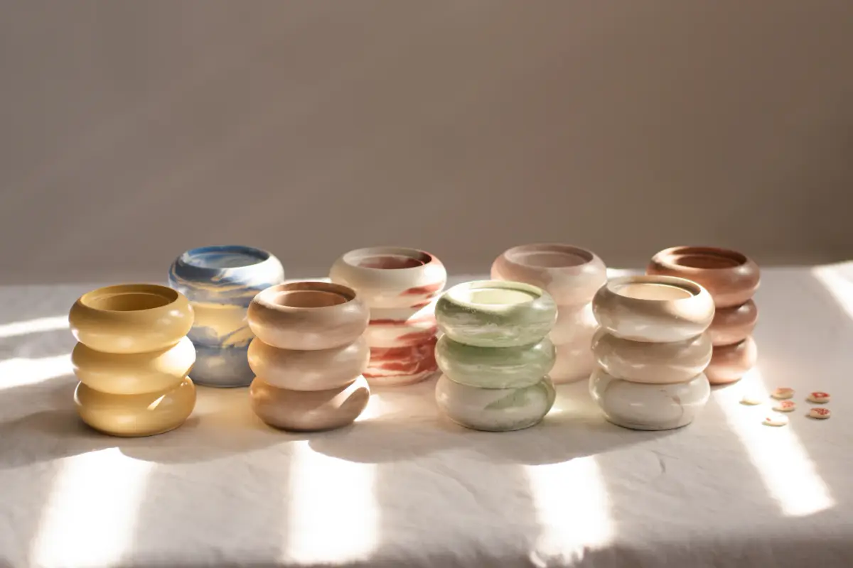 A row of stacked, ring-shaped ceramic vessels in pastel glazes on a linen cloth
