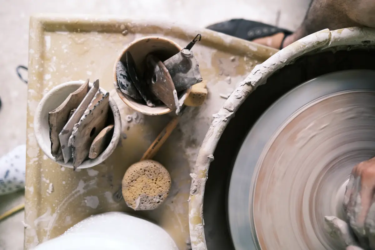 A potter shaping a pot on a spinning wheel, tools and clay around it
