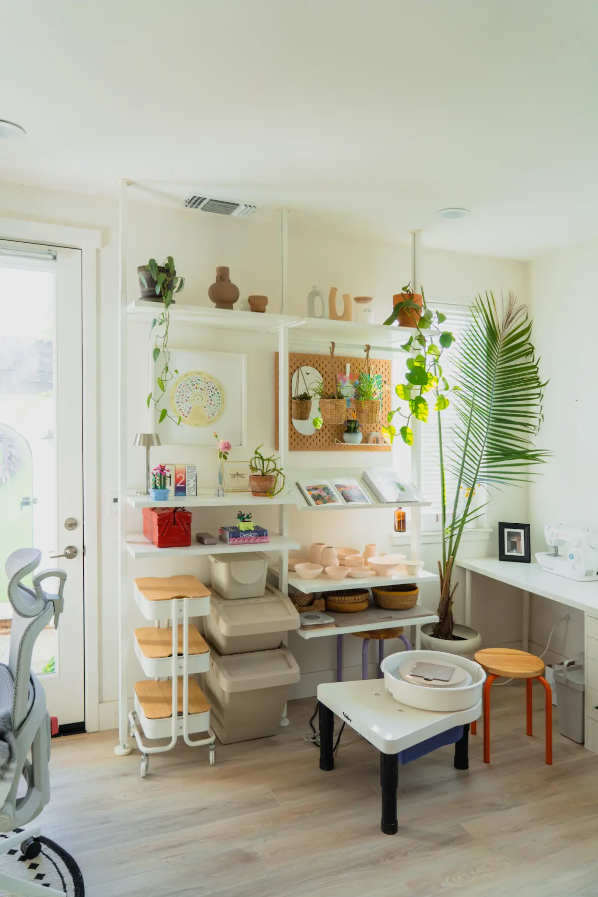 The bright Kiln & Clay studio with a wheel, shelves of drying pots and a large palm
