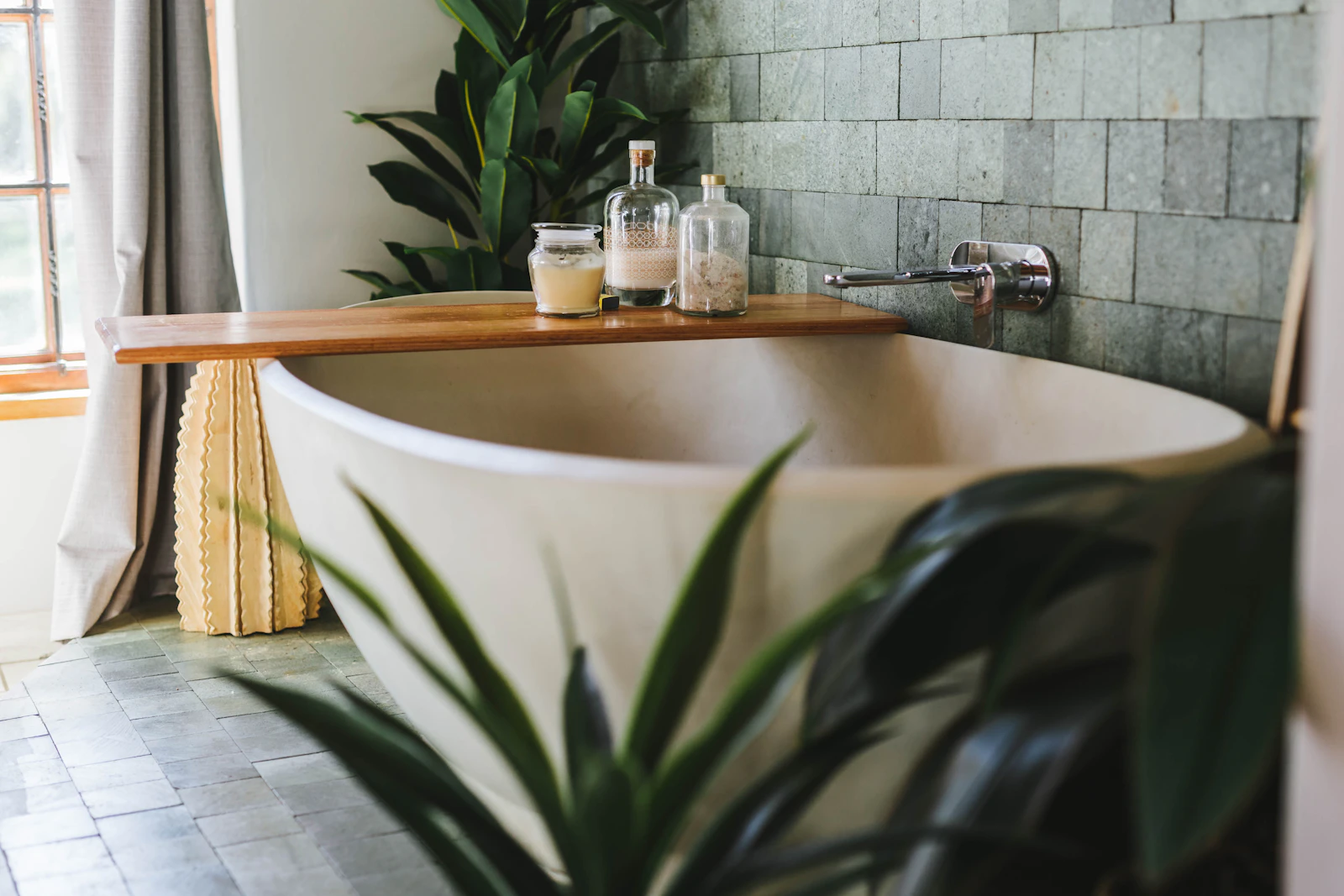 After: a deep freestanding bath against green tiles, with a wooden shelf and plants