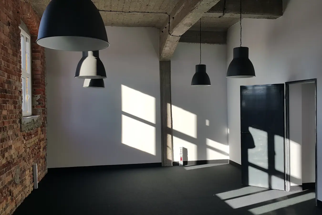 Before: an empty industrial space with a brick wall, black pendant lamps and sunlight on the floor
