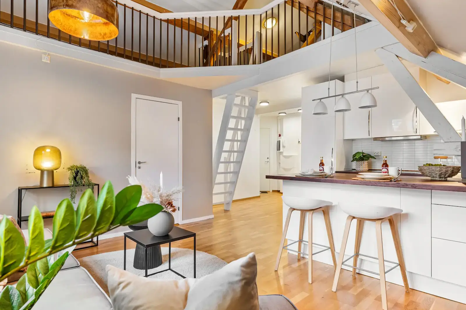 After: a bright open living space with a mezzanine, an open kitchen and a sofa under tall windows