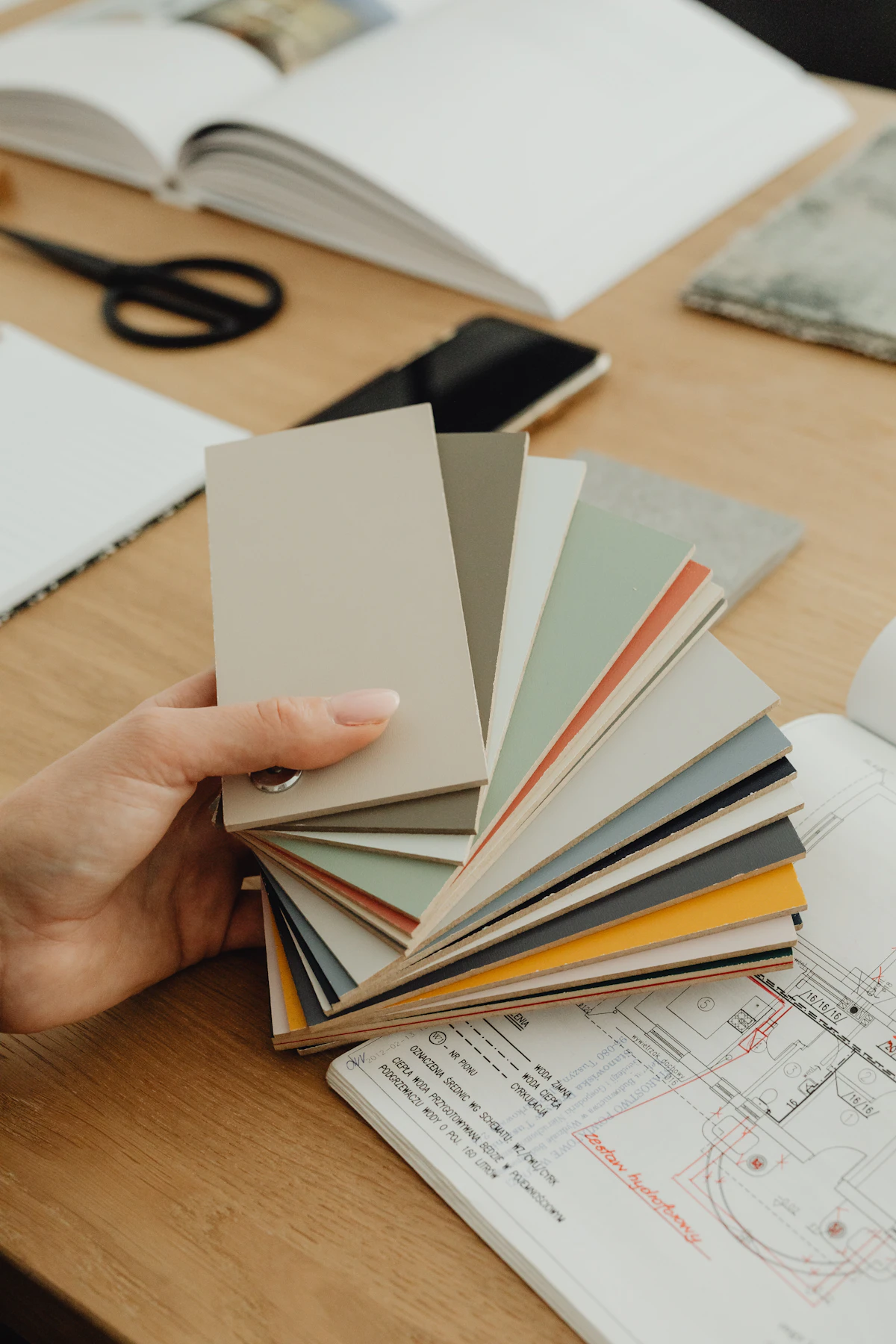 A designer's hand fanning out colour swatches over blueprints