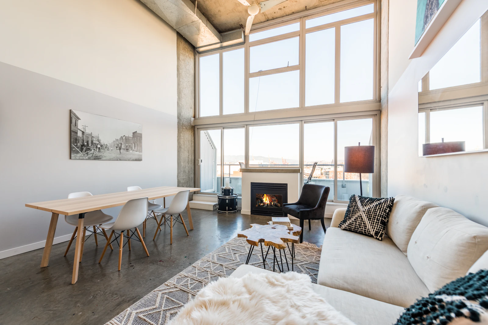 A light living room with tall windows, a fireplace, a long dining table and a cream sofa