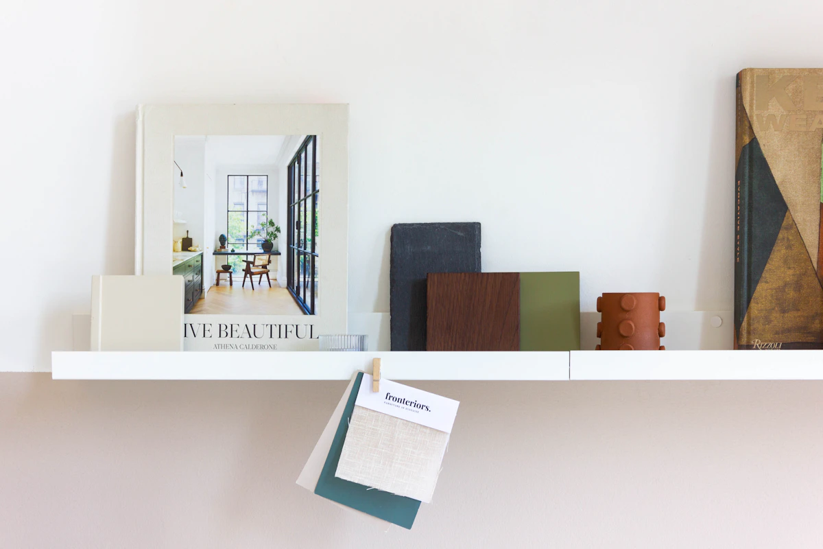 A studio shelf with books, framed prints and material samples