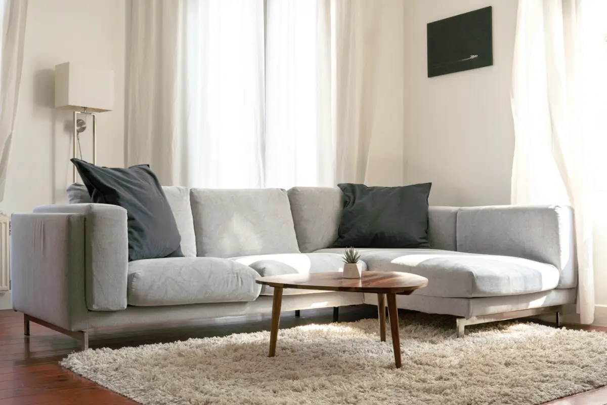 A light grey L-shaped corner sofa with dark cushions, a round wooden coffee table and a shaggy rug