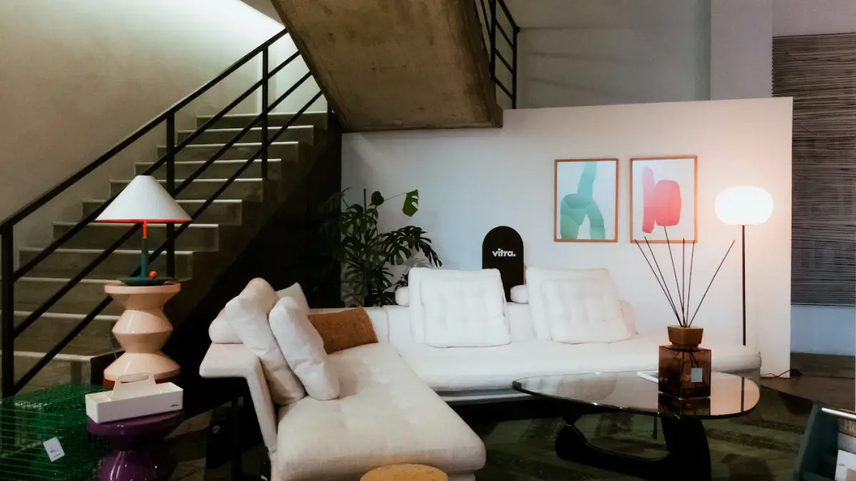 A bright showroom with a long white sofa, framed prints and an open staircase behind