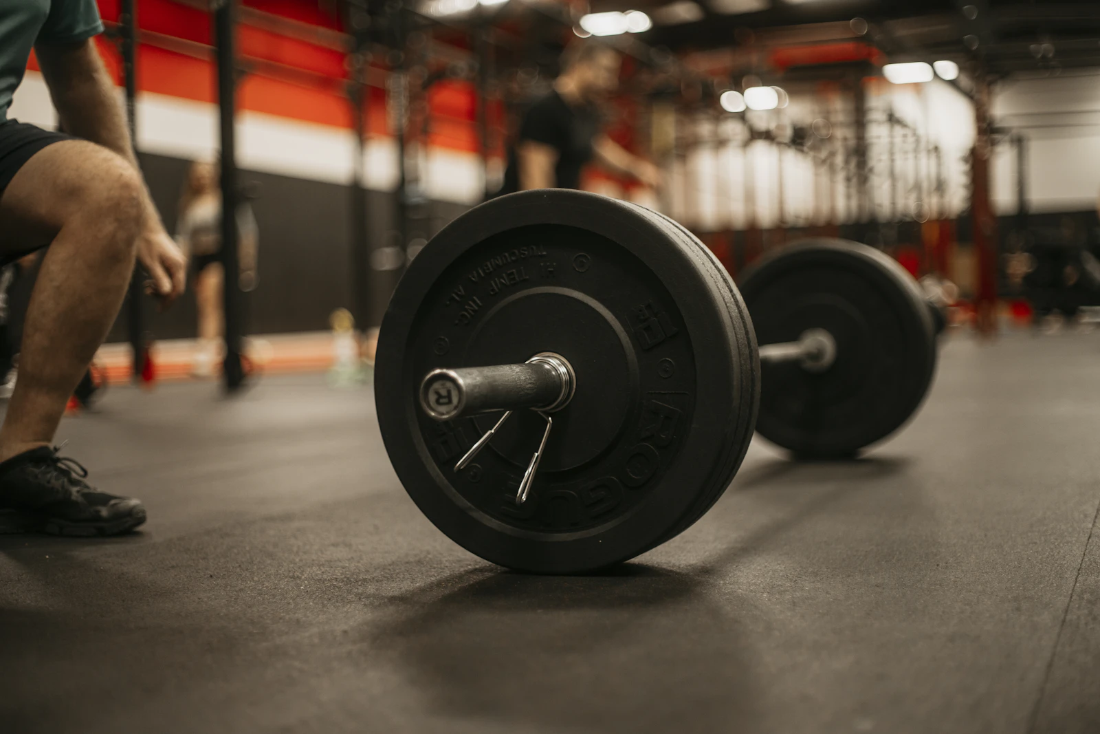 A lifter squatting beside a loaded barbell in a dark gym