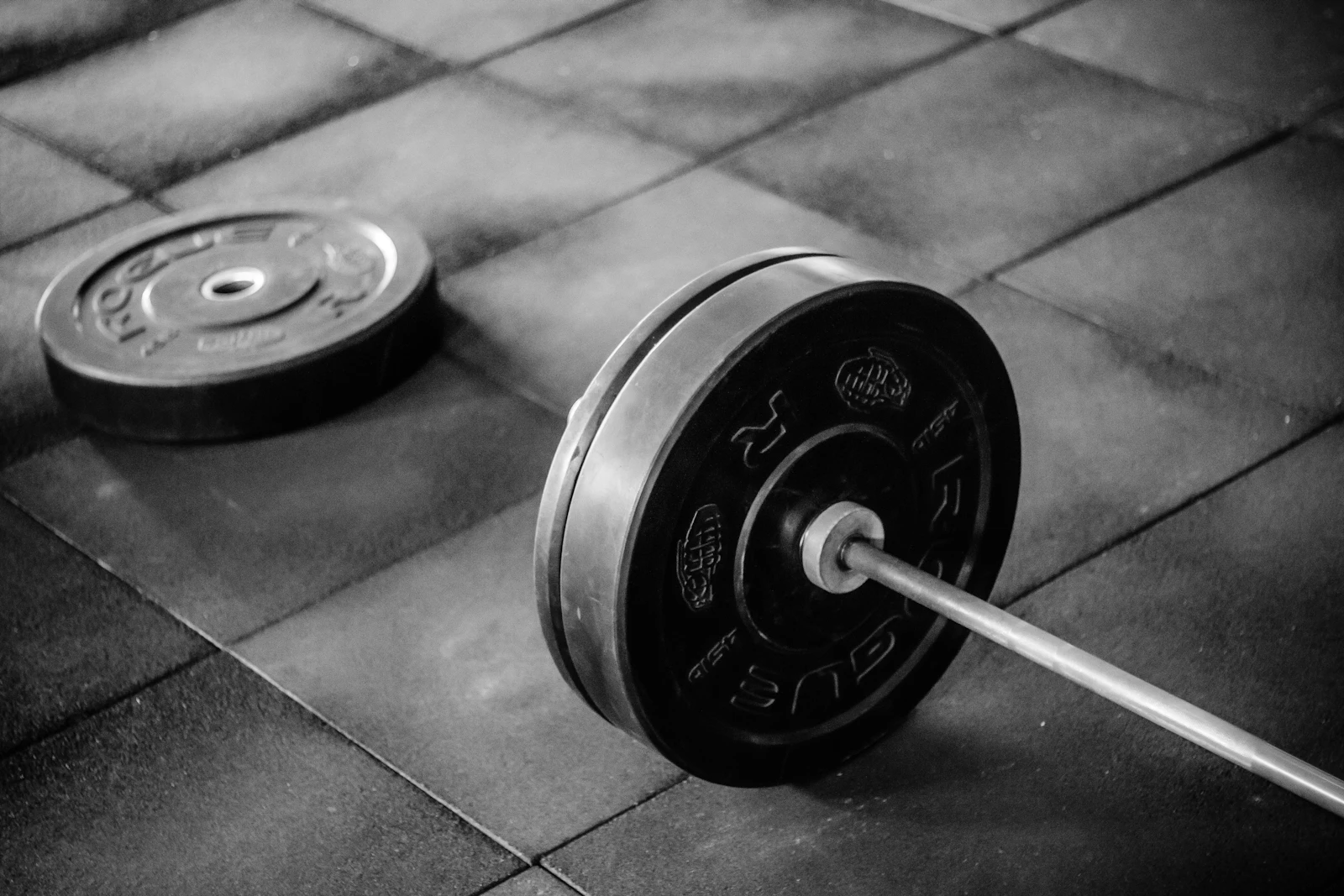 A loaded black barbell plate on a gym floor, in black and white