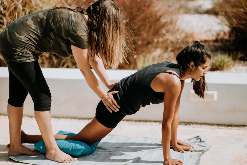 A teacher guiding a student into a pose on a yoga mat