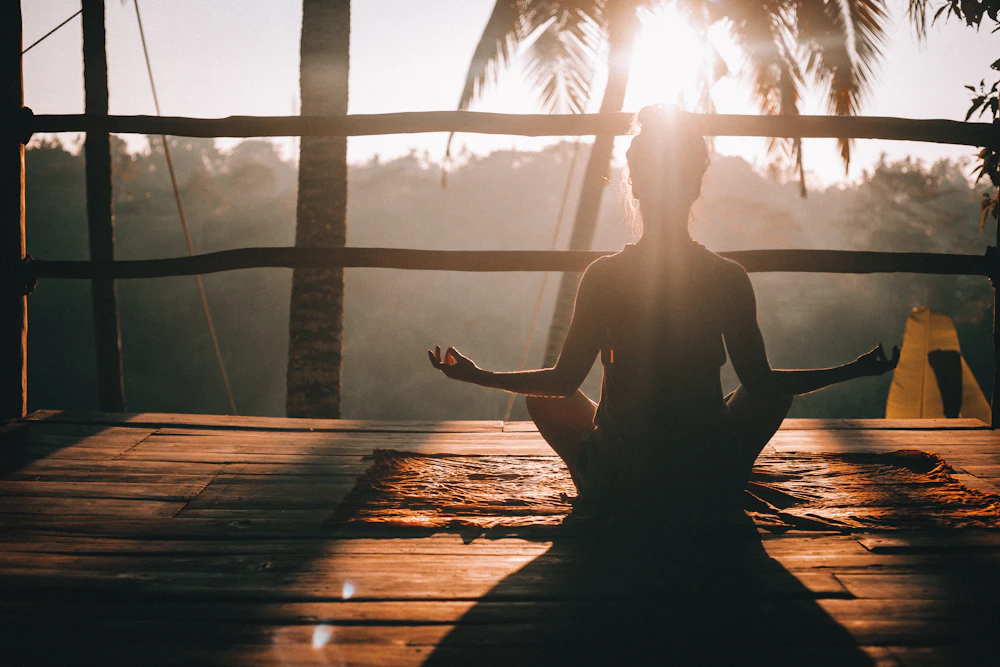 A woman in silhouette practicing yoga on a wooden dock at sunrise