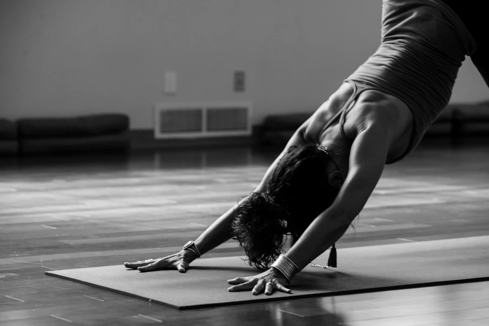 A woman folding forward in a slow, quiet yoga pose, in black and white