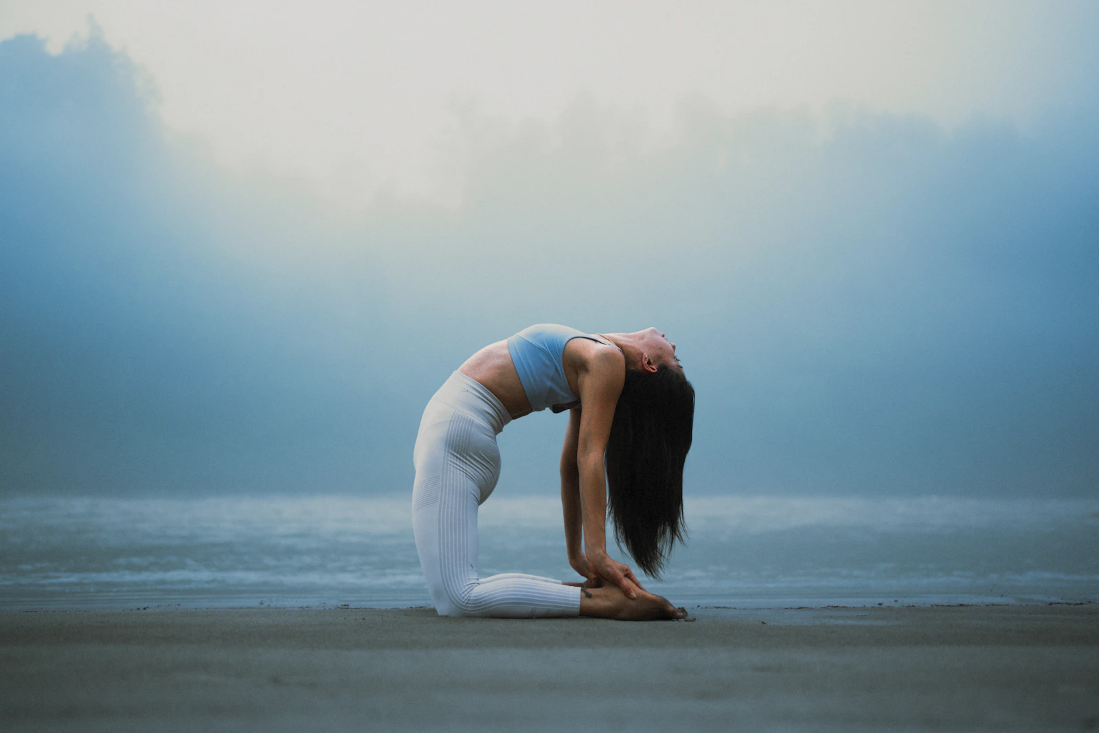 A woman in a deep backbend on a misty beach