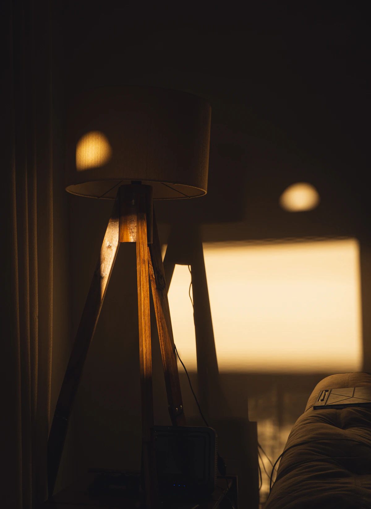 A wooden tripod floor lamp casting warm light in a dim room