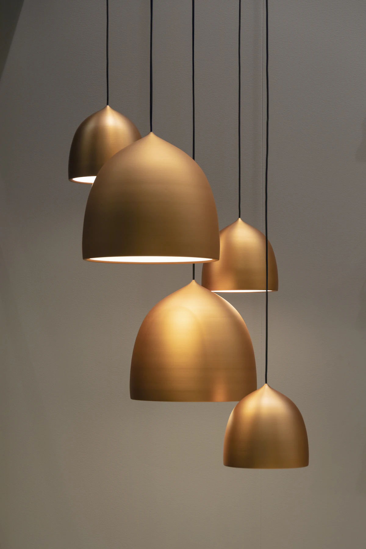A cluster of brass dome pendants hanging at different heights, all switched on