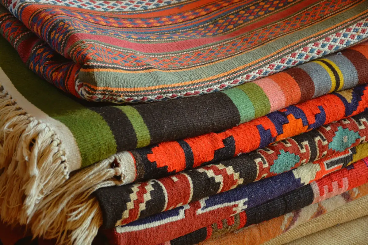 A stack of folded handwoven kilims in red, orange, green and blue with fringed edges