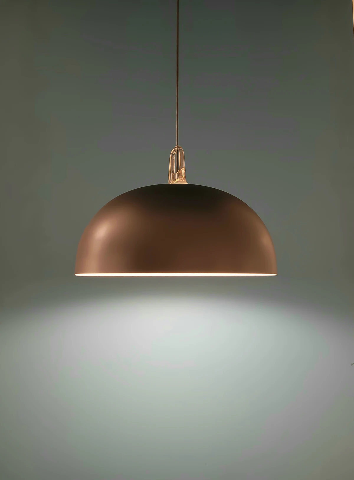 A brass dome pendant switched on, throwing light down onto a grey wall