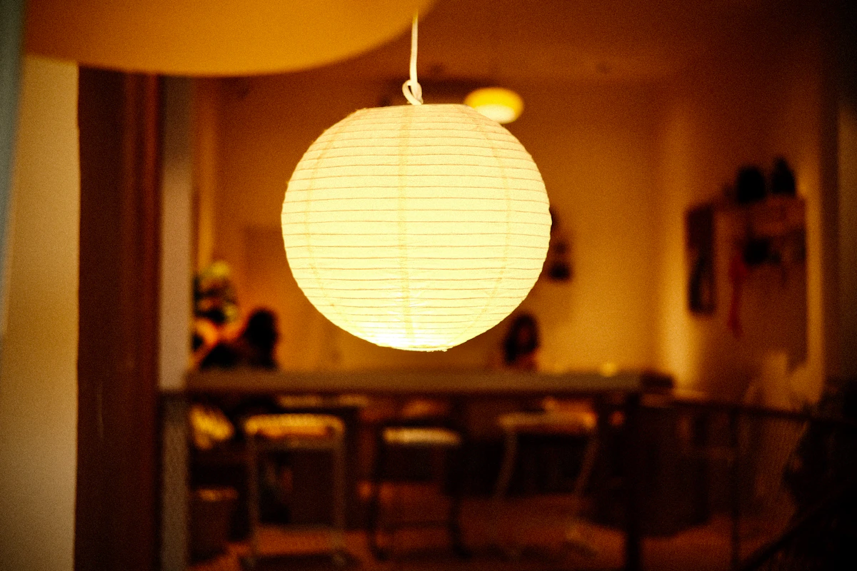 A lit round paper globe pendant glowing above a table in a warm, dim room