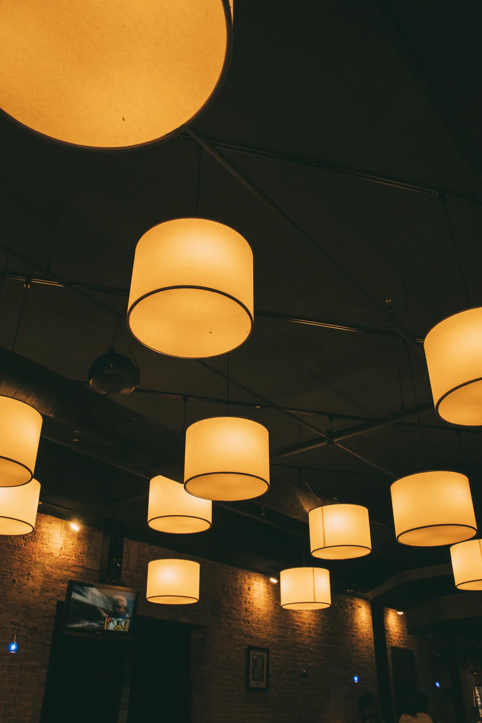 Rows of glowing drum-shaped pendant lights hanging from a dark ceiling