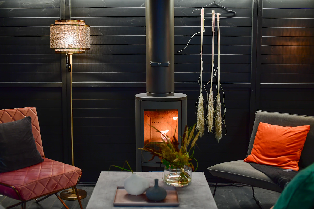 A dark showroom corner with a lantern floor lamp, two armchairs and a wood stove