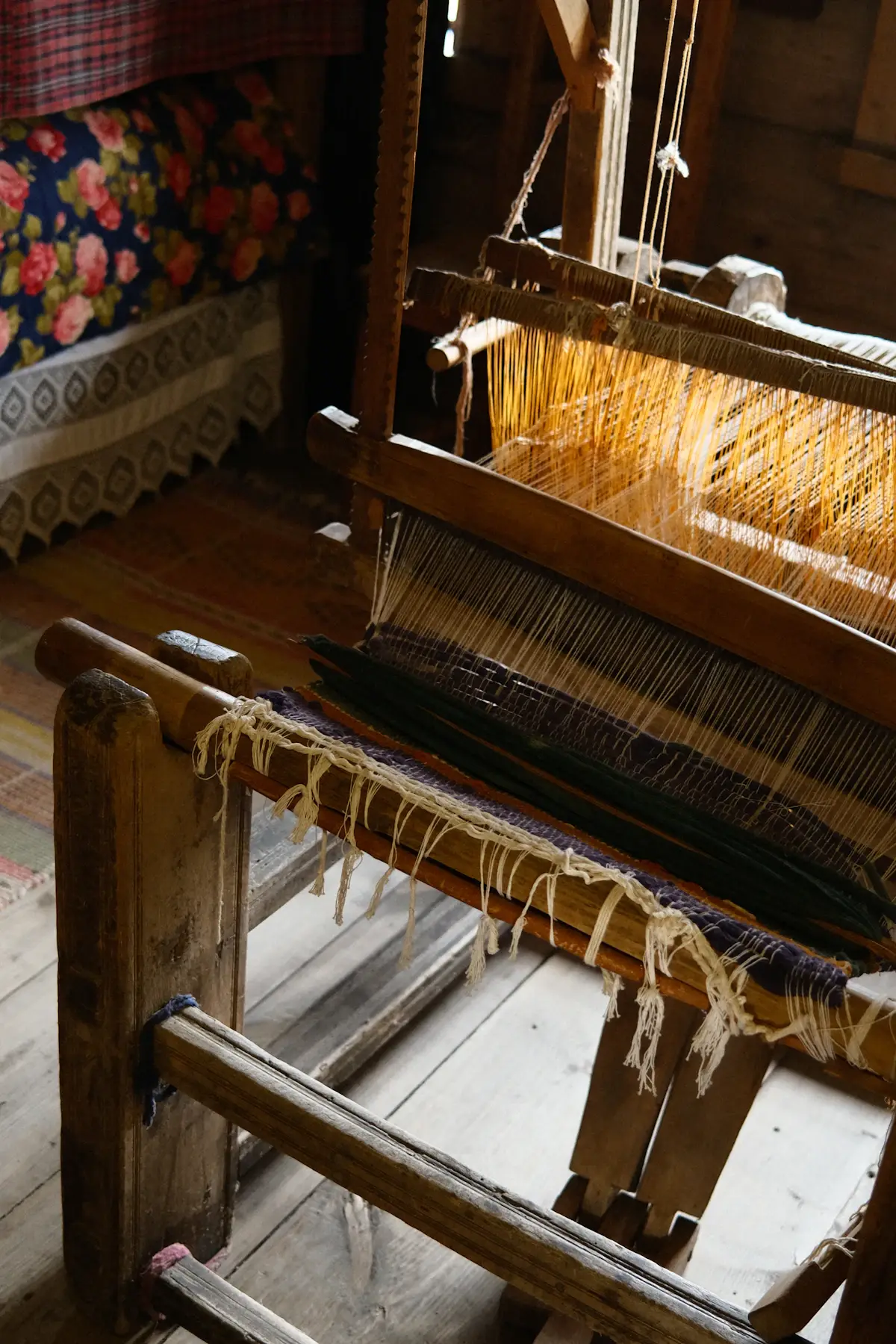 An old wooden hand loom with cream warp threads in warm workshop light