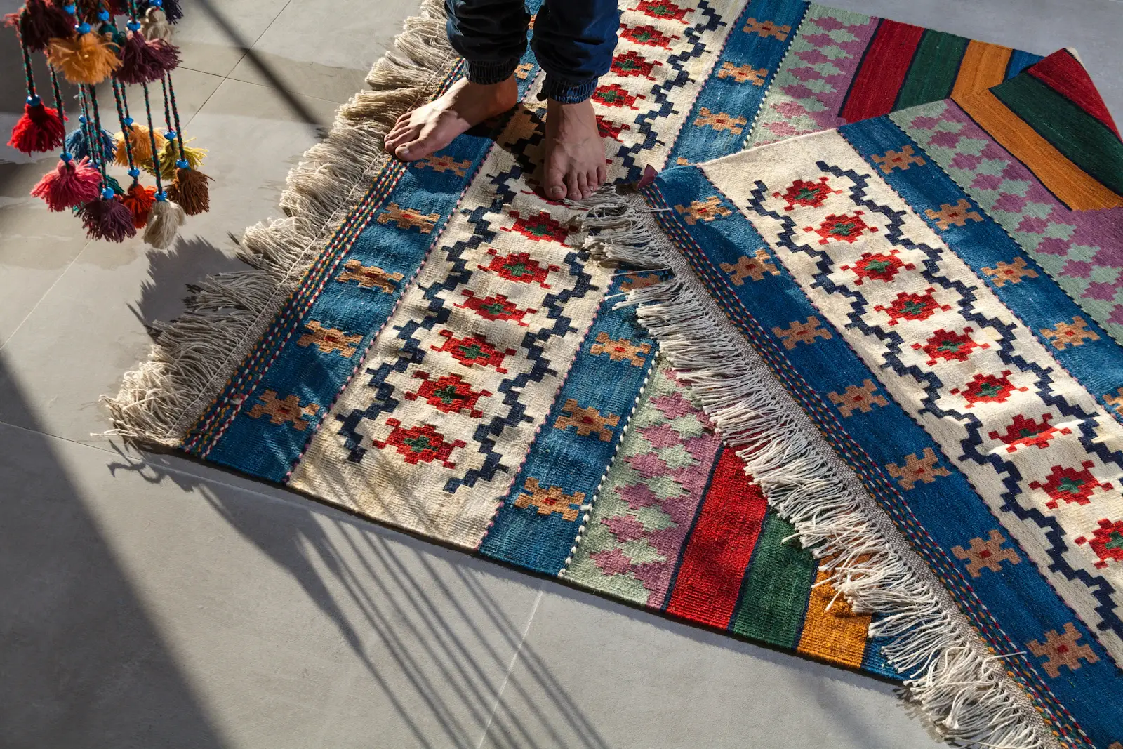 Bare feet on a kilim in indigo, cream and red with knotted fringes on a pale floor